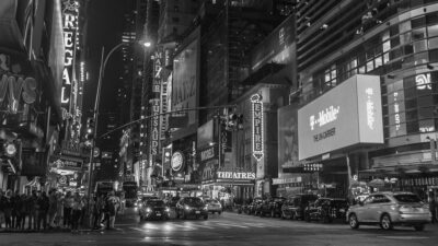 Black and white photo of a busy city intersection surrounded by billboards