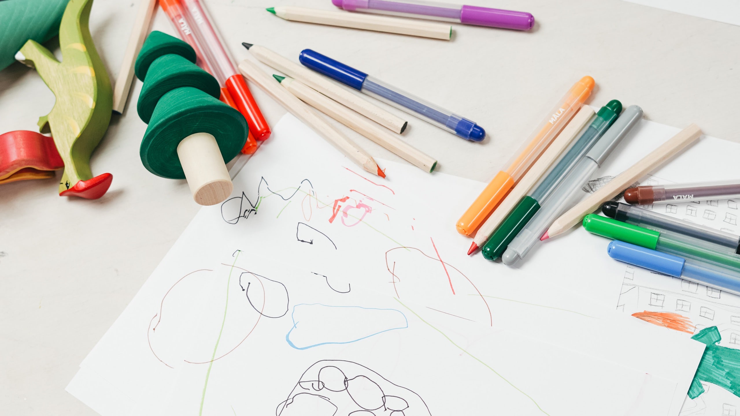 Pens and toys on a table, a child's drawing on paper